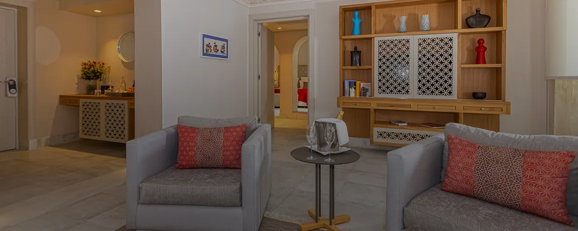 Salon de la Suite avec fauteuils gris, coussins rouges et bibliothèque en bois